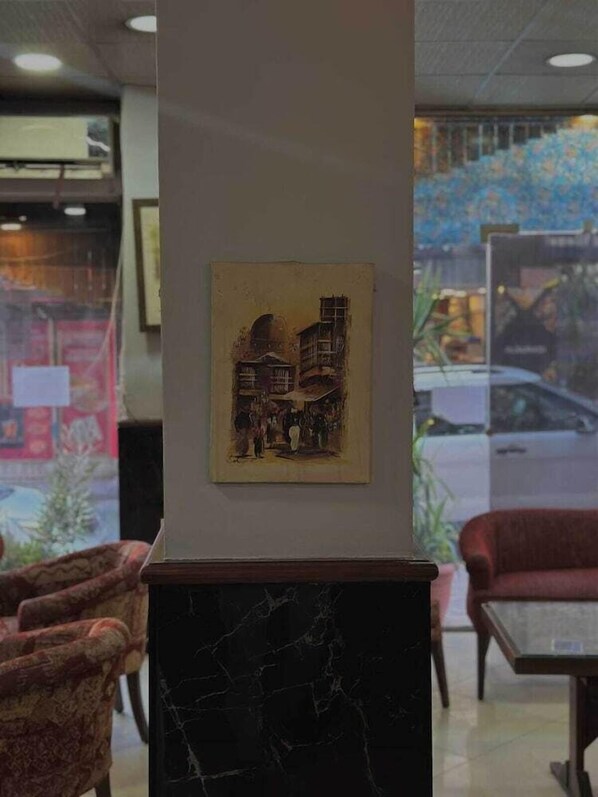A lobby with a marble column, a framed artwork depicting a building, and a view of the street outside. - The Amman Pasha Hotel (Amman)