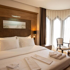 A hotel room with a large bed, a painting on the wall, a chair, and a desk. - Hotel Vrbak (Novi Pazar)