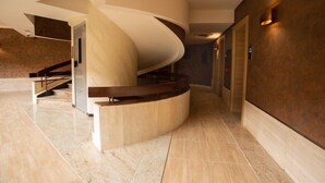 Eine moderne Hotelhalle mit einer geschwungenen Treppe, Marmorböden und einer warmen Wandgestaltung.