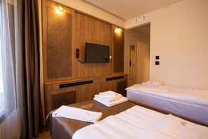 Hotellihuone, jossa on kaksi sänkyä, seinään kiinnitetty televisio ja peili seinällä.