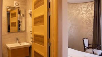 A hotel room with a wooden door, a bathroom with a sink and mirror, and a bed with towels.