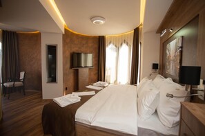 A hotel room with a large bed, a television, a desk with a lamp, and a painting on the wall. - Hotel Vrbak (Novi Pazar)