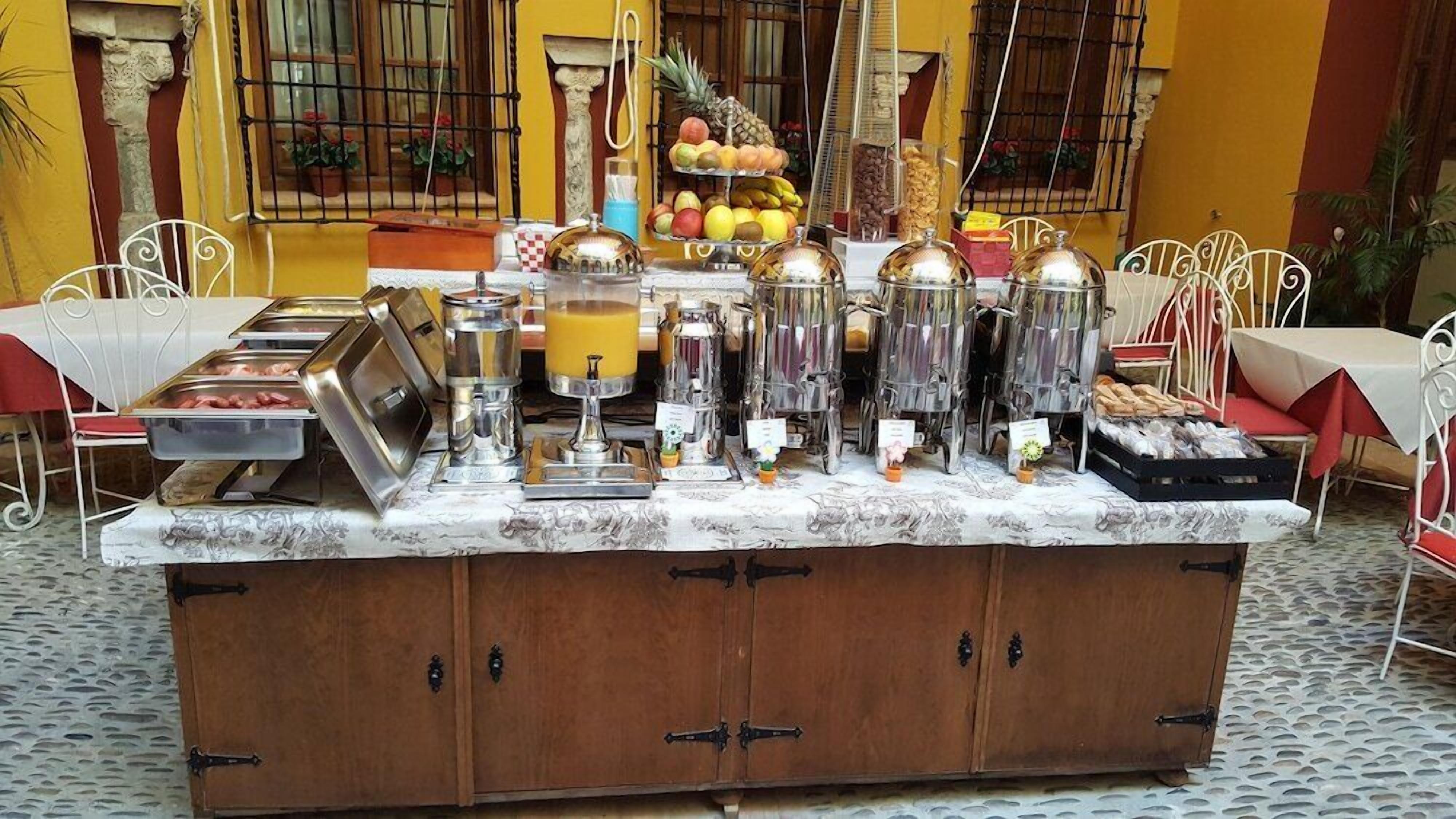 A breakfast bar with various food items and beverages, surrounded by white metal chairs and tables.