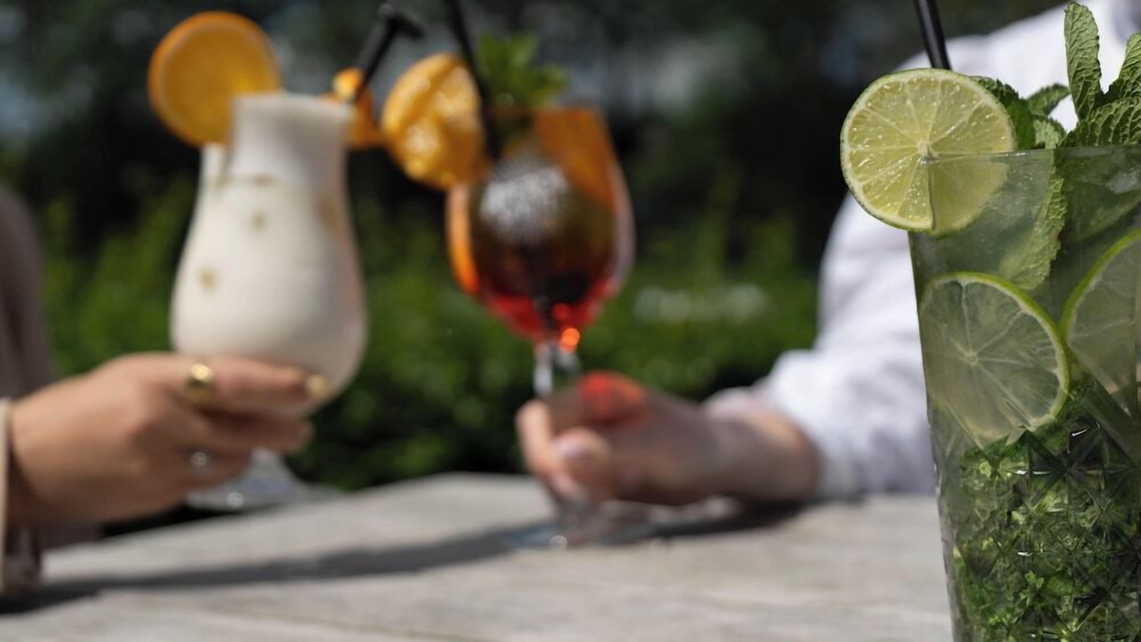 Two people holding drinks at an outdoor table with a drink in a glass and a pitcher.