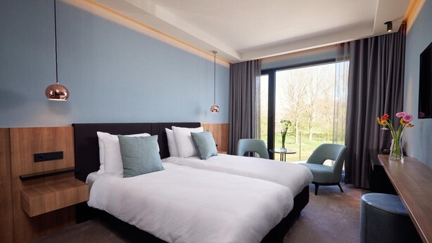 Ein modernes Hotelzimmer mit zwei Betten, einem Schreibtisch und Blick ins Freie.