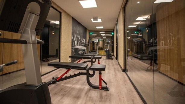 A gym with cardio machines, benches, and mirrors on the walls. - Hotel Gorinchem (Gorinchem)