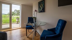 Ein modernes Wohnzimmer mit Glastisch, blauen Stühlen, einer Blumenvase und einem Gemälde an der Wand.