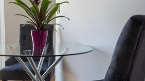 Ein modernes Zimmer mit einem Glastisch, einem dunkelgrauen Stuhl und einer Topfpflanze.