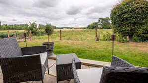 Eine Terrasse im Freien mit Korbmöbeln und Blick auf eine Wiese.