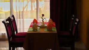 A dining table set for two with a vase of flowers, a candle, and a glass of water. - Royal Garden Hotel (Sohar)