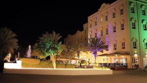 A multi-story hotel with a courtyard, palm trees, and outdoor seating areas. - Royal Garden Hotel (Sohar)