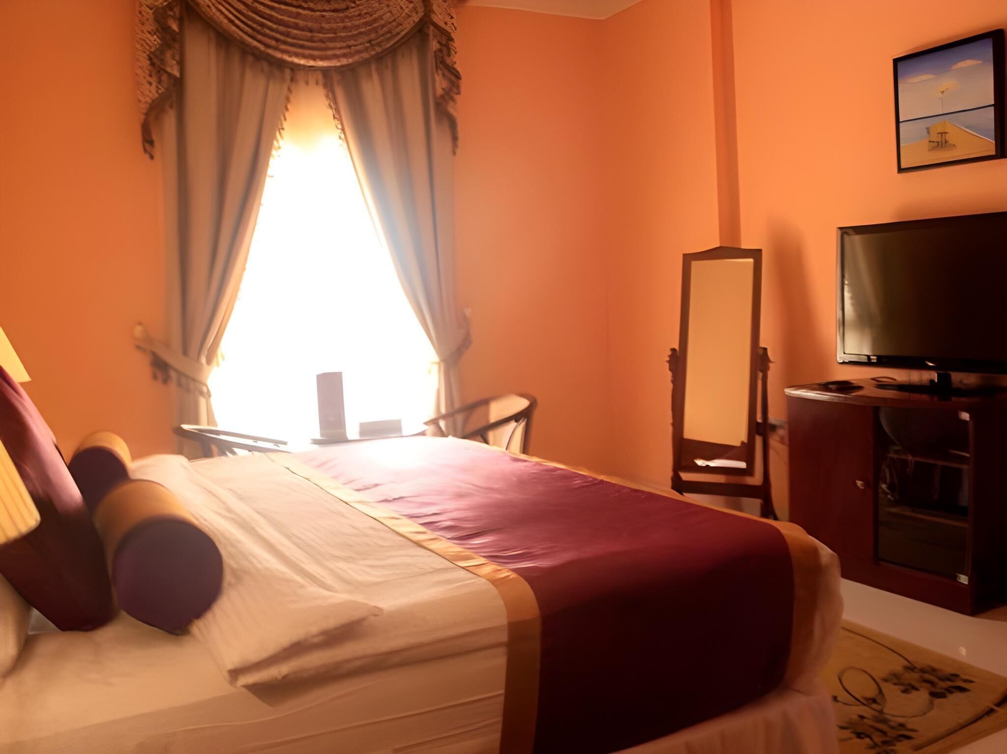 A hotel room with a bed, a television, a mirror, and a window with curtains.