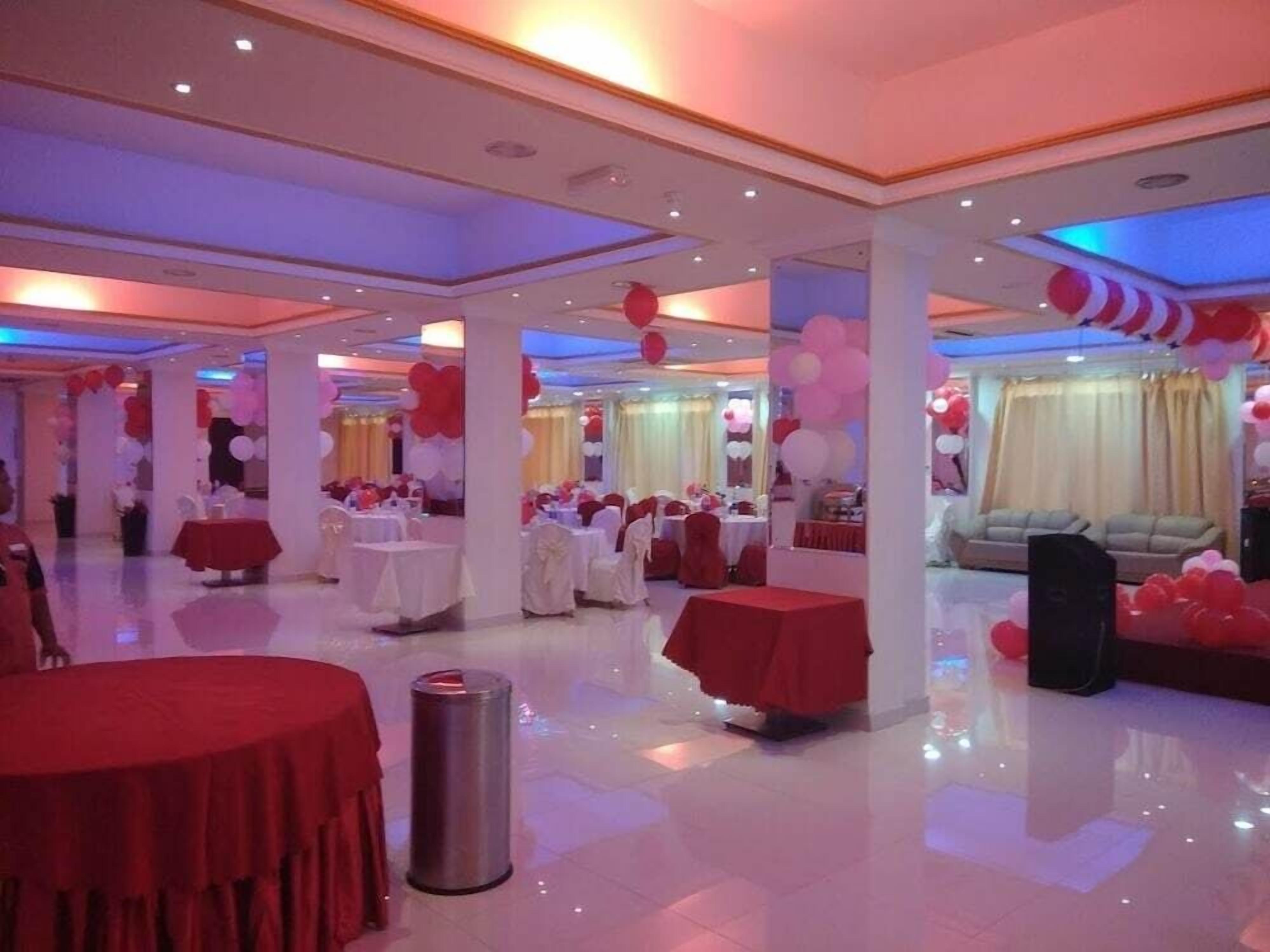 Un grand hall spacieux avec de nombreuses tables rondes recouvertes de nappes rouges, des chaises blanches et des ballons rouges et blancs.