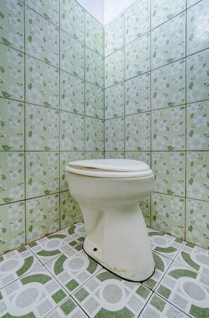 A bathroom with a toilet, green floral tiles on the walls, and patterned floor tiles. - OYO 113676 Wisma Al-fahmi Syariah (Jalaksana)