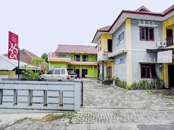 A multi-story building with a green and yellow facade, a covered parking area, and a gated entrance. - OYO 113676 Wisma Al-fahmi Syariah (Jalaksana)