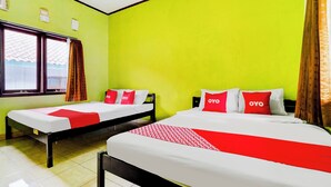 Ein Hotelzimmer mit zwei Einzelbetten, jeweils mit einer rot-weißen Bettdecke und Kissen mit dem Aufdruck "OYO". Der Raum hat eine leuchtend grüne Wand und ein Fenster mit Vorhängen.