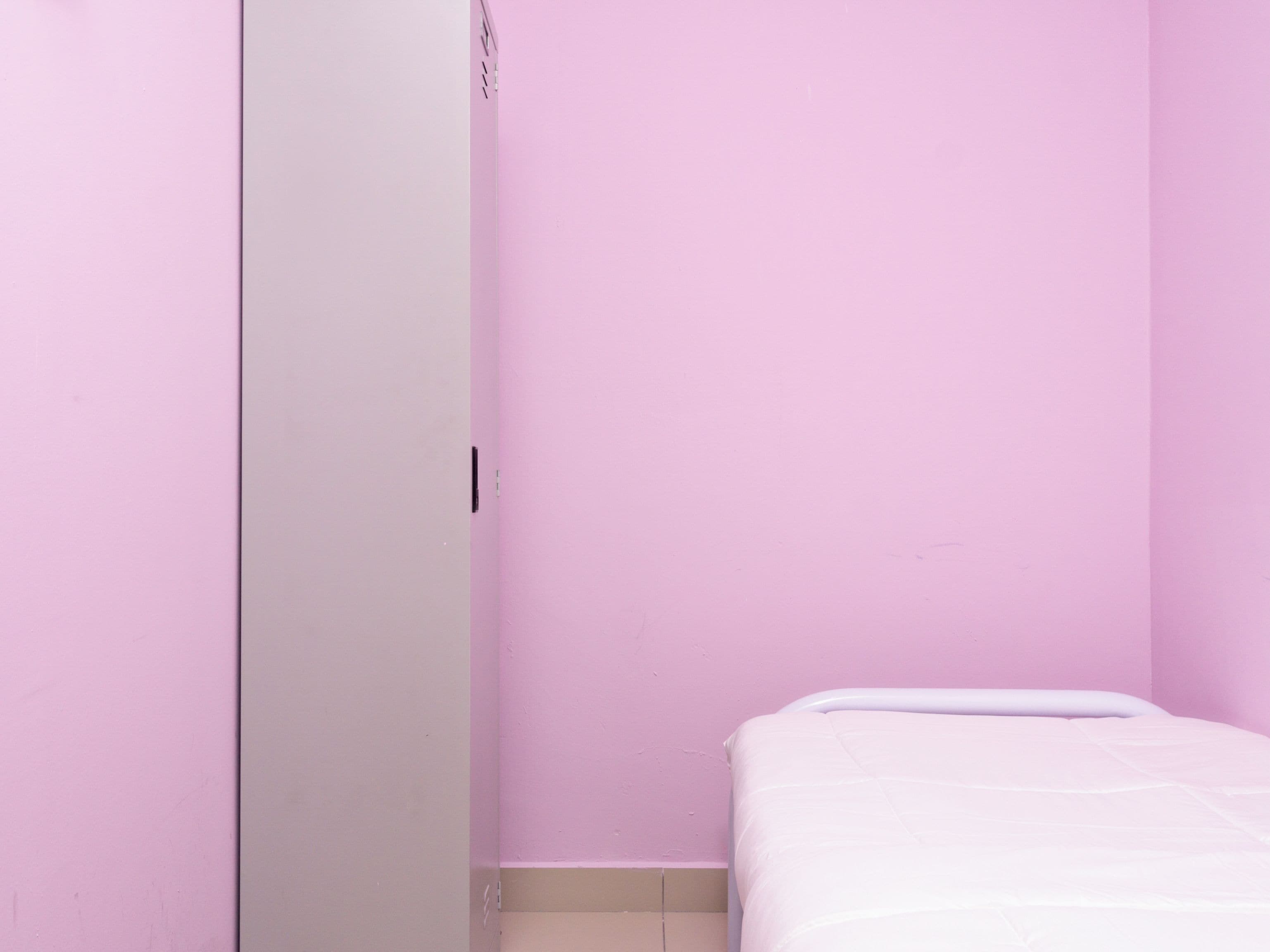 Une chambre avec un lit simple, une armoire blanche et des murs roses.
