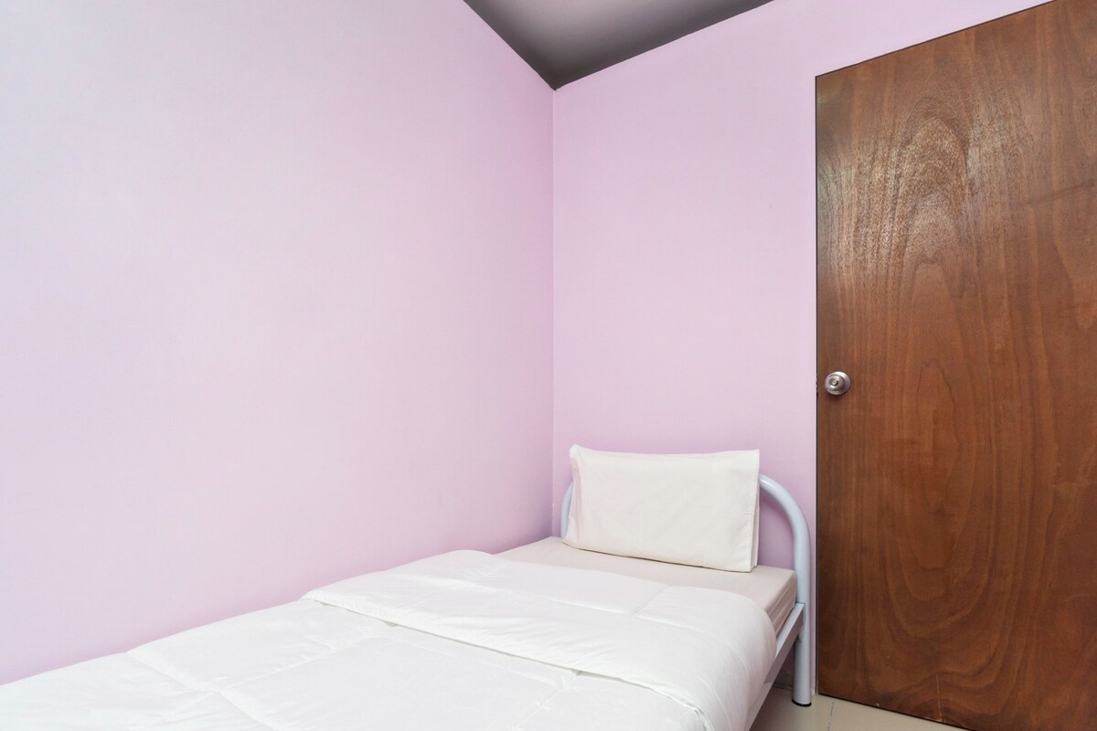 Een eenpersoonsbed met een wit matras en kussen in een kamer met roze muren en een houten deur.