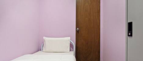 A small, single-bed room with a wooden door and a white bedspread.