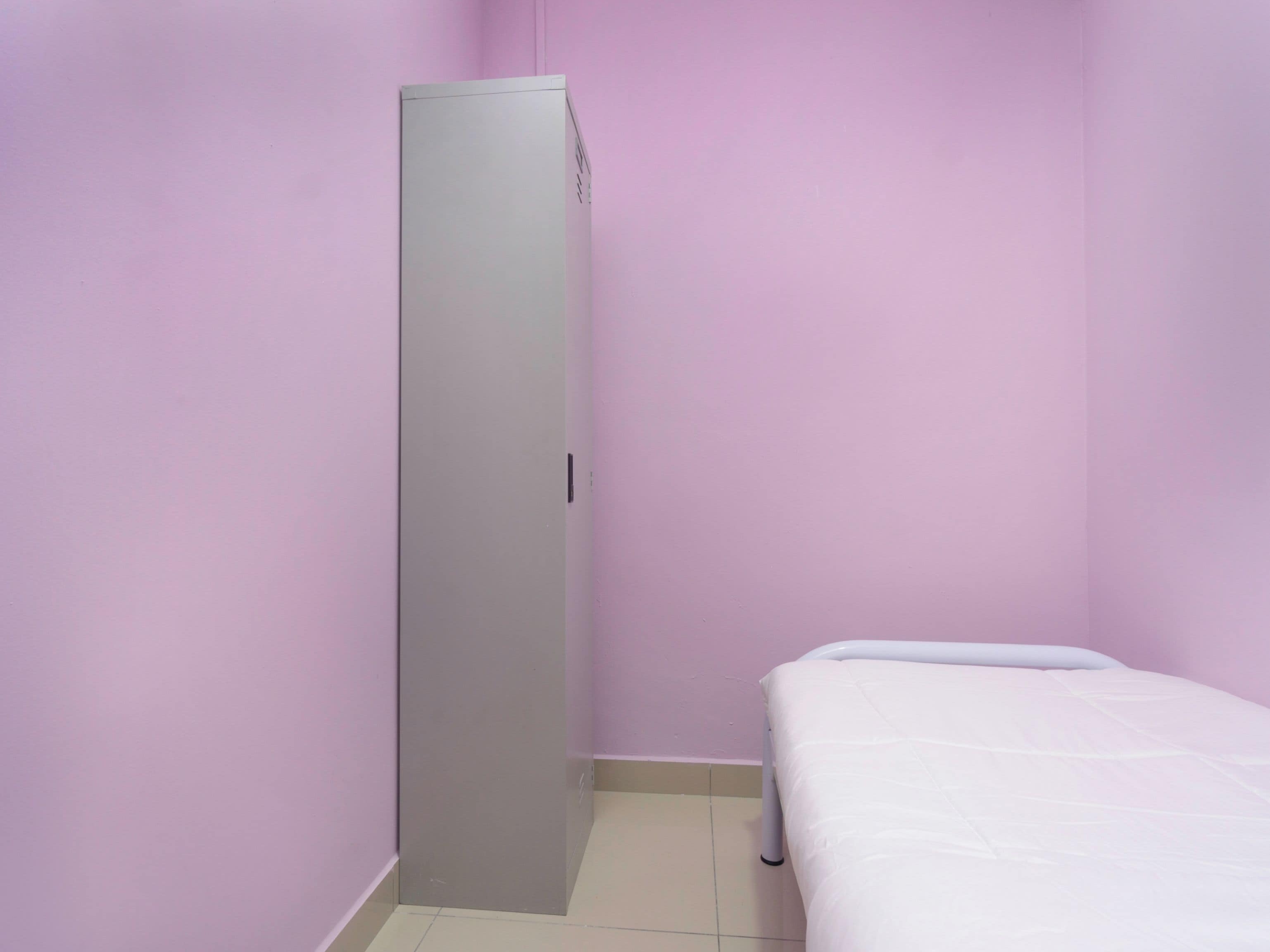 Ein kleines Zimmer mit einem Einzelbett, einem Kleiderschrank und einem Fliesenboden.