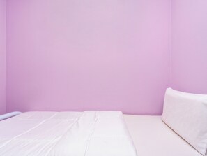 Ein Zimmer mit einem Bett an einer rosafarbenen Wand, einem weißen Kissen und einer weißen Matratze.