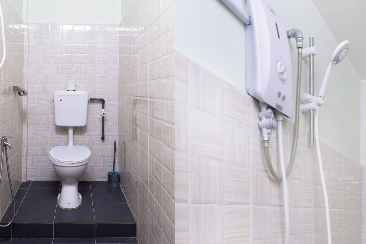 Une salle de bain équipée de toilettes, d’une douche et d’un porte-rouleau de papier toilette fixé au mur.