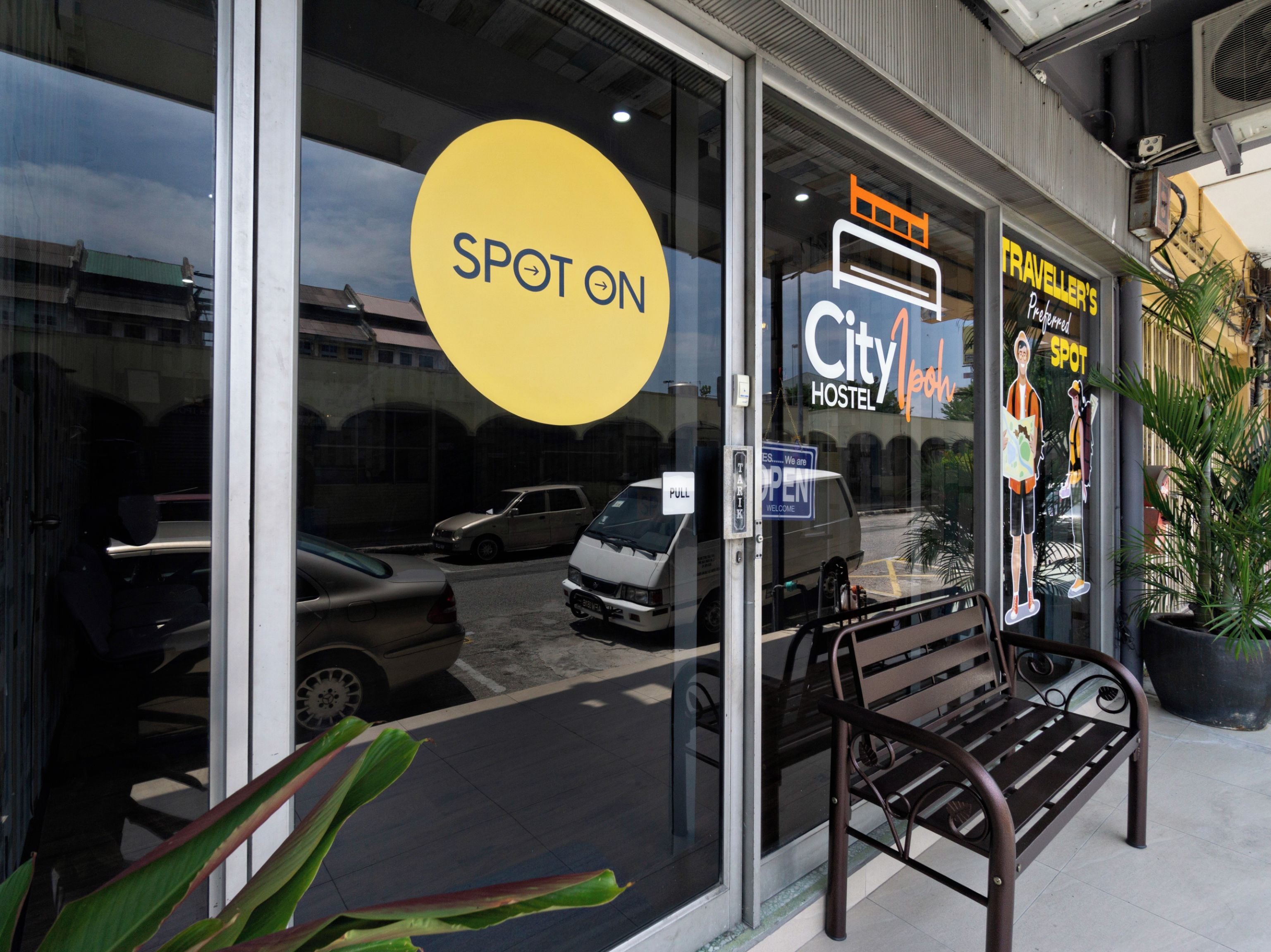 En hotelindgang med et stort, gult skilt med teksten 'SPOT ON', et skilt der siger 'City Hostel' og et skilt med 'Traveller's Spot'.