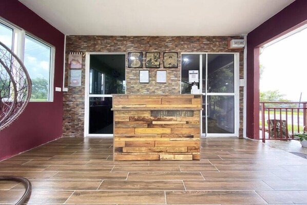 Un área de recepción con mostrador de madera, pared de piedra y grandes puertas de cristal que dan a un espacio exterior.