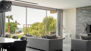 A modern living room with a large window, grey sofas, a dining table, and a stone fireplace. - Bavaro Beach Dakhla (Dakhla)
