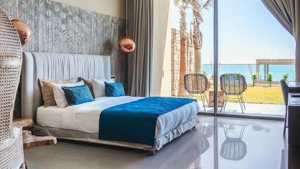 A modern bedroom with a bed, a large window, and a view of the beach. - Bavaro Beach Dakhla (Dakhla)