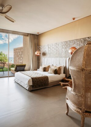 A bedroom with a bed, a wicker chair, a stone wall, and a view of the outdoors. - Bavaro Beach Dakhla (Dakhla)