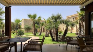 A covered outdoor seating area with tables and chairs, surrounded by palm trees and a well-maintained lawn, leading to a building with stone walls. - Pietra D'acqua Natural Retreat and Spa Resort (Scicli)