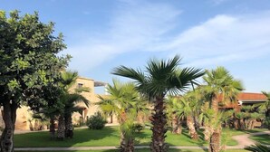 A courtyard with palm trees, a pathway, and a building with a red roof. - Pietra D'acqua Natural Retreat and Spa Resort (Scicli)