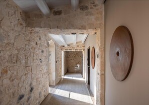Un couloir en pierre avec une porte en bois et un objet circulaire en bois accroché au mur.
