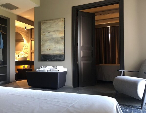 A hotel room with a bed, a seating area with a table, a large abstract painting, and a door leading to another room. - Pietra D'acqua Natural Retreat and Spa Resort (Scicli)