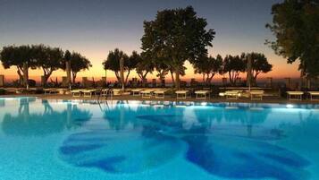 A swimming pool with lounge chairs and trees in the background during twilight.