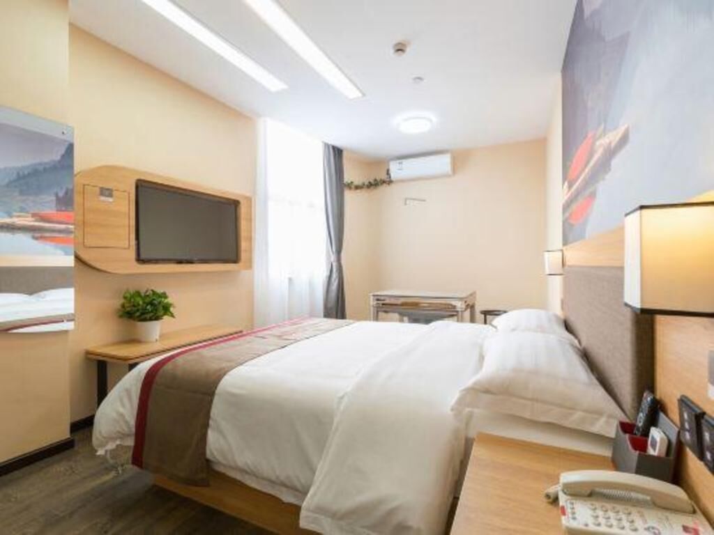 A hotel room with a bed, bedside table, lamp, and a mounted television.