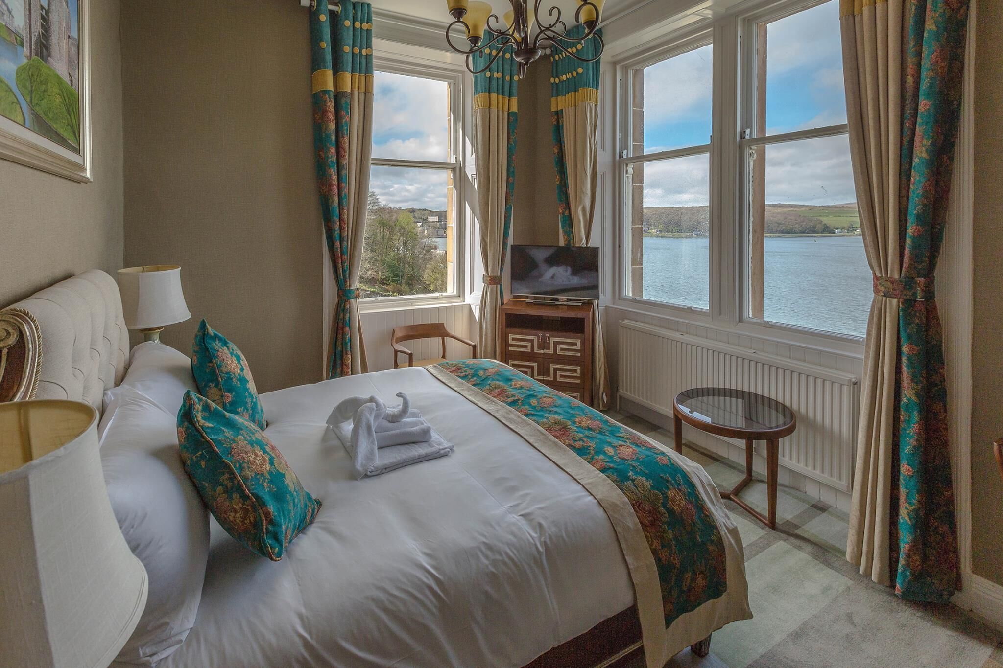 A hotel room with a bed, a TV, a chair, a table, and a view of a lake.