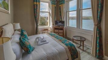 A hotel room with a bed, a TV, a chair, a table, and a view of a lake.