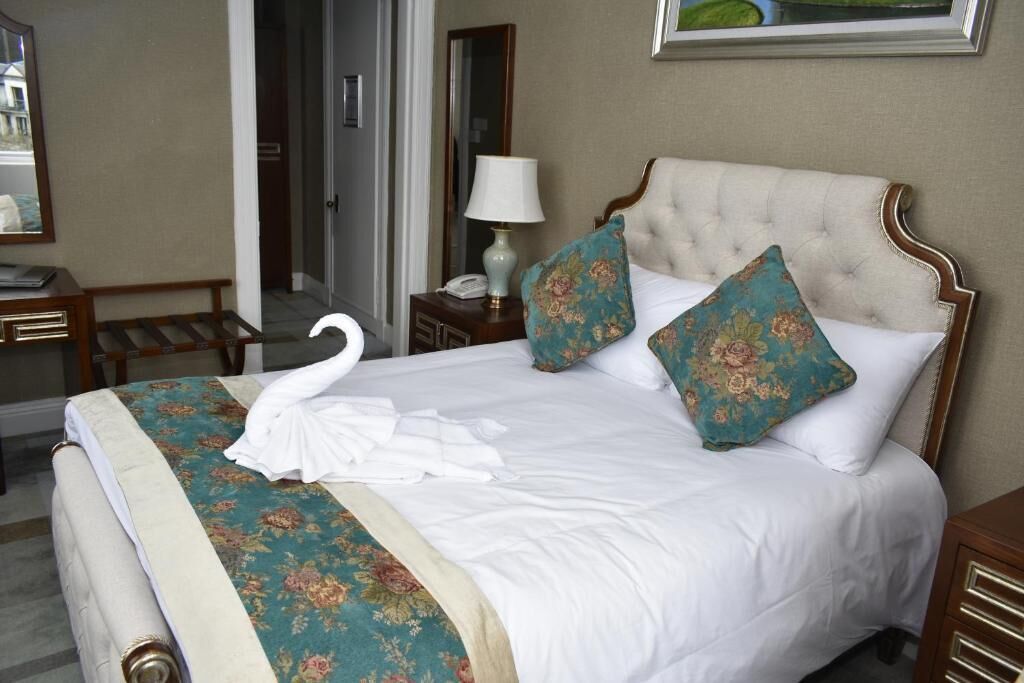 A neatly made bed with a floral bedspread, two decorative pillows, and a swan-shaped towel.