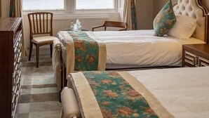 A hotel room with two beds, a view of the sea through a large window, a wooden chair, and a dresser. - Glenburn Hotel (Rothesay)