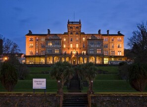 Un grande hotel storico con un ingresso maestoso, numerosi piani e un giardino curato.
