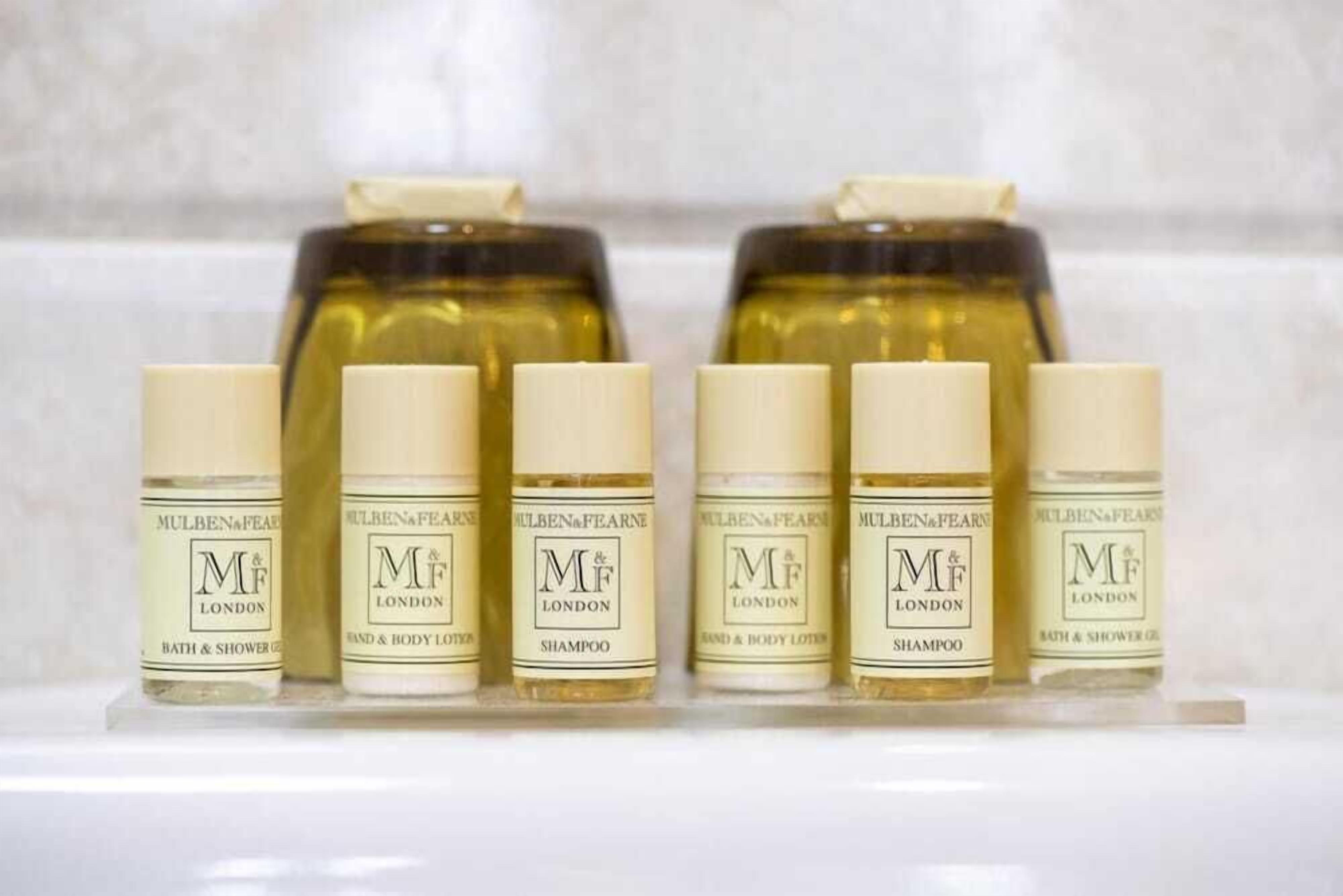 A row of six bottles of M&F London bath and shower gel, with two larger bottles of M&F London shampoo behind them.