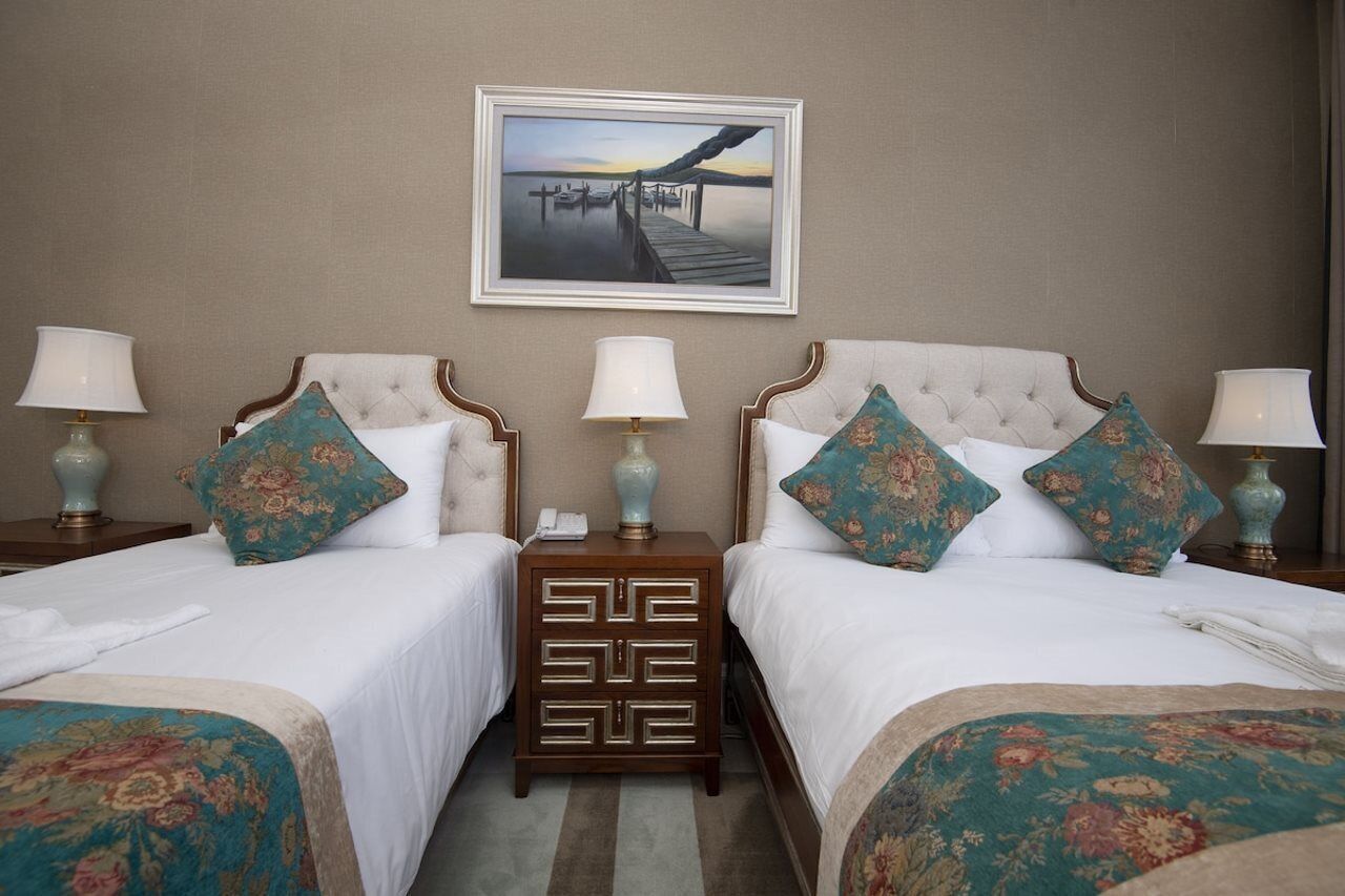Een hotelkamer met twee bedden, elk met een bijpassend nachtkastje, een ingelijst schilderij aan de muur en een lamp op elk nachtkastje.
