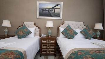 Een hotelkamer met twee bedden, elk met een bijpassend nachtkastje, een ingelijst schilderij aan de muur en een lamp op elk nachtkastje.
