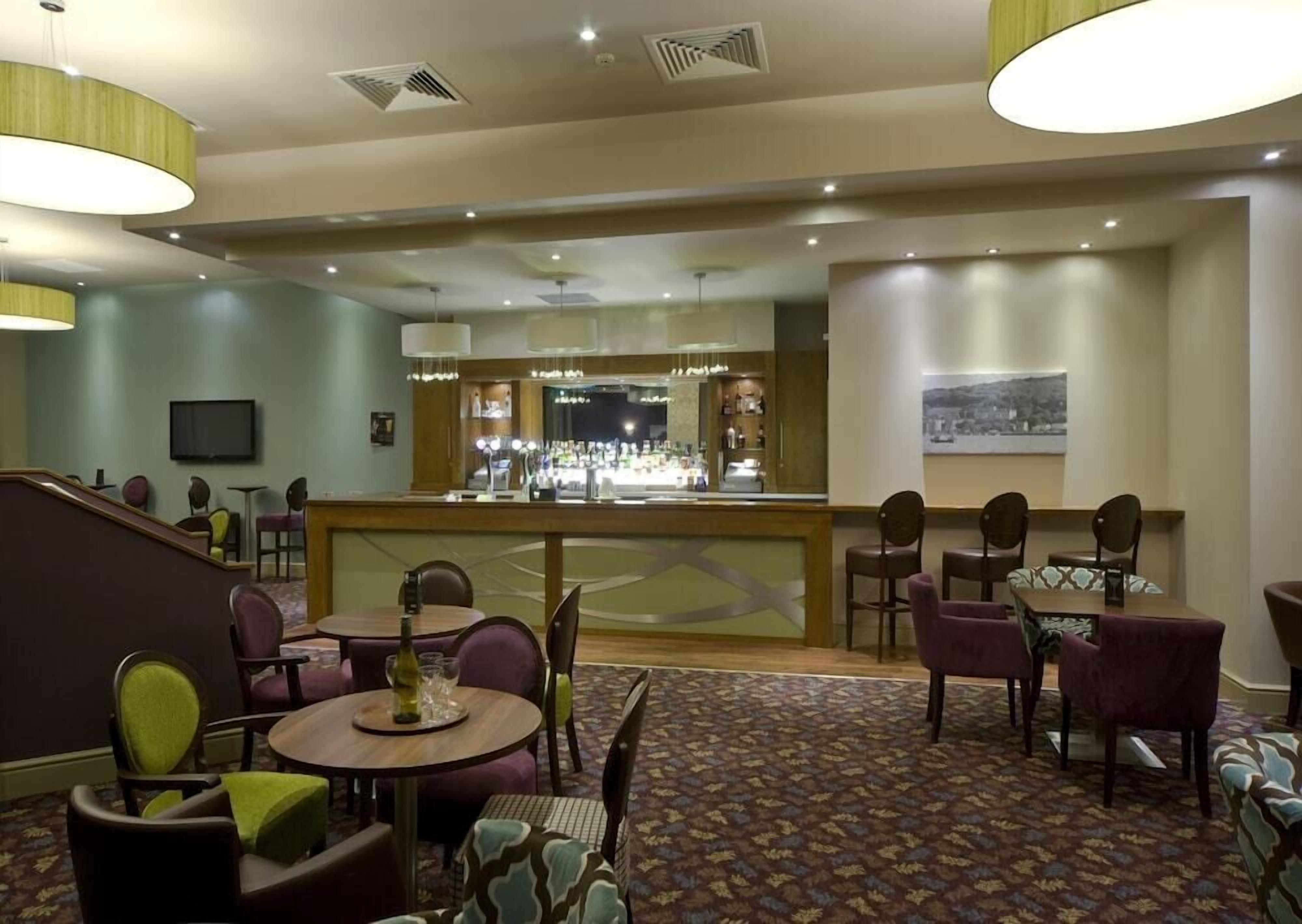 Een hotel lobby met een bar, zitgedeelte en een kamerbreed tapijt met patroon.