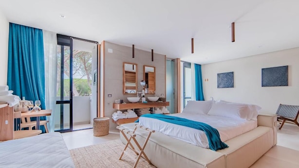 A modern hotel room with a large bed, a desk with a chair, a bathroom with a sink and mirror, and a view of the outdoors. - Cumeja Beach Club Hotel (Cellole)