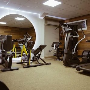 Een fitnessruimte met diverse trainingsapparaten, waaronder loopbanden, hometrainers en krachtapparaten.