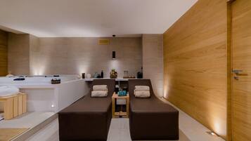Un'elegante sala spa moderna con una grande vasca da bagno, due poltrone reclinabili, un tavolino con articoli da toilette e una parete in legno.