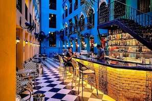 Un espace bar avec un sol à carreaux, des tabourets de bar et un comptoir où sont exposées différentes bouteilles.
